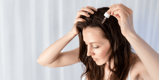 Woman applying hair oil serum to scalp with dropper for healthy hair care routine banner image.