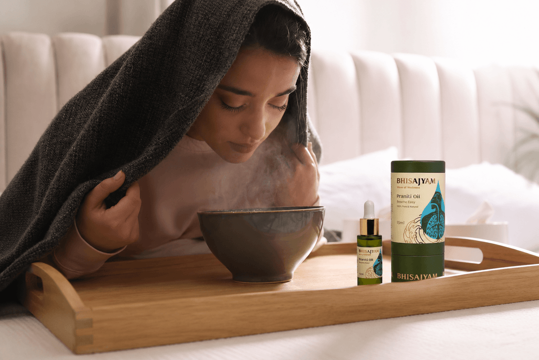 Woman taking steam inhalation under a blanket with Bhisajyam Praniti Oil placed beside the bowl, promoting natural relief for cold, cough, blocked nose, and sinus congestion.